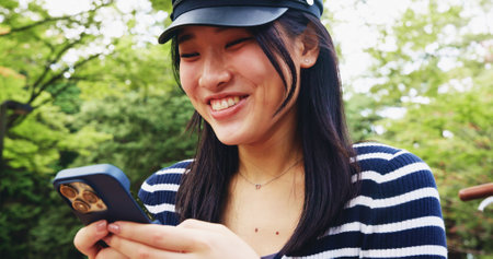 Face, phone and smile with woman in park for adventure, sightseeing or travel to explore Japan. App, holiday and social media with happy tourist person typing message outdoor in nature for vacationの写真素材