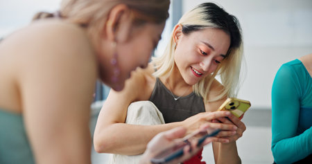 Cellphone, friends and women in dance studio with networking, communication or browsing social media. Smile, phone and Japanese ballerinas watching online video for classic technique at rehearsal.の写真素材