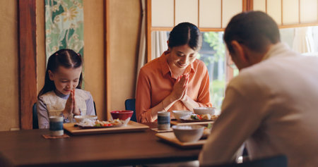 Japanese family, pray or food with dinner tradition for faith, gratitude or bow together at home. Mother, father or daughter with thankful culture or respect for meal, snack or eating at dining tableの写真素材
