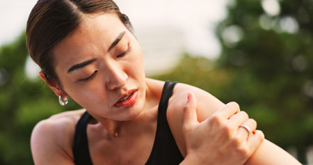 Outdoor, woman and fitness with shoulder pain from exercise strain with muscle ache and injury in Japan. Female person, workout and active with inflammation or sore for self care, health or wellbeingの写真素材