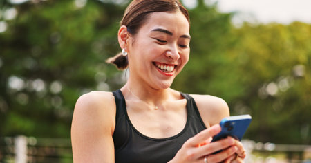 Outdoor, woman and laugh for fitness with smartphone on app for tracking health progress in Japan. Female person, hands and happy on internet or online with memes on social media and text messageの写真素材