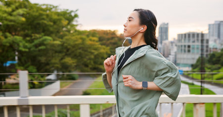 Japanese woman, running and earphones in city of sport exercise, marathon training and listen to music. Female athlete, cardio and workout practice of endurance performance, wellness and Japan bridgeの写真素材