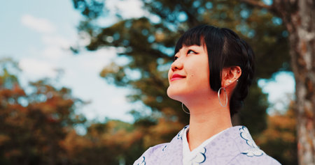Green, park and woman in kimono with smile, thinking and relax for outdoor sightseeing adventure in nature. Culture, inspiration and Japanese girl in garden for traditional spring festival with treesの写真素材