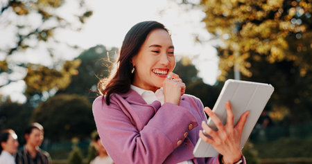 Business, woman or laughing with tablet in park for funny text message, social media meme or online joke. Professional, japanese person or digital app for streaming service or reading web informationの写真素材