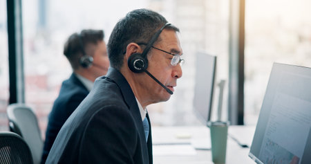 Call center, mature man and computer with customer service for technical support, FAQ assistance or help desk. Japanese agency, consultant and microphone for contact us, CRM advice and consultingの写真素材