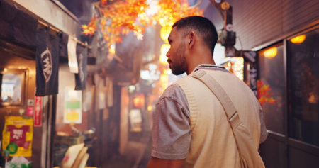 Night market, back and travel with Japanese man in city for shopping, vacation and festival. Culture, traditional holiday and walking with person in alley for Street food, tourism and heritageの写真素材