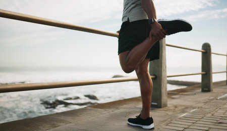 Man, running and warm up legs at beach, stretching and outdoor nature for fitness. Male person, sea promenade and footwear for exercise preparation, getting ready and cardio workout by ocean wavesの写真素材