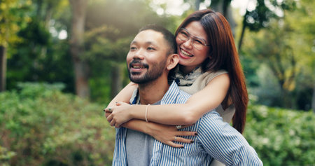 Japan, outdoor and couple with piggy back, love and bonding together with relationship. Romance, care and man carrying woman with trust, smile and marriage with nature, travel and commitmentの写真素材