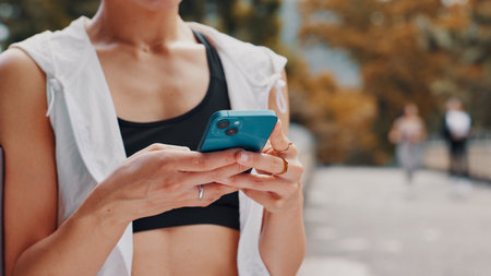 Hands, person and phone of fitness in city for communication, sports application and travel. Athlete, typing and mobile with social media, reading blog and contact chat of commute directions in Japanの写真素材