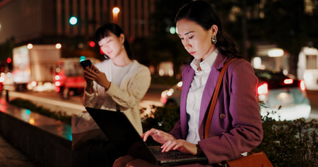 Night, woman and laptop in city for business, research deadline and connectivity in Yokohama. Japanese workaholic, typing or computer on dark sidewalk for late work, commitment or networking at bokehの写真素材