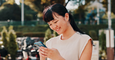 City, online and happy Asian woman with phone for communication, social media and networking. Travel, weekend and person on smartphone for chatting, mobile app notification and website in Japanの写真素材