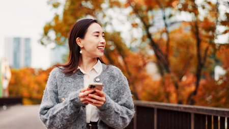 Thinking, phone and happy woman at park for travel, text or message on app in Japan. Smile, mobile and Asian person outdoor for dream, planning vacation and post on social media profile on internetの写真素材