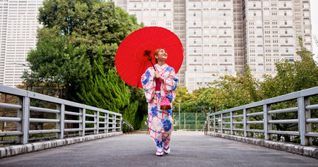 City, umbrella and Japanese woman with fashion, sightseeing and travel on urban bridge. Street, kimono and parasol with walking, outdoor and journey with smile, style and traditional Asian dressの写真素材
