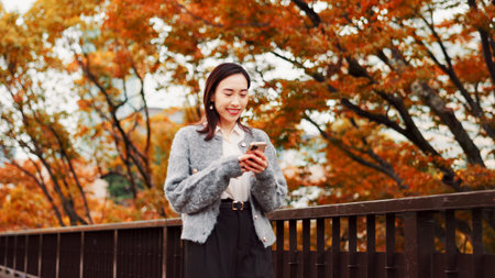 Typing, smile and woman with phone at park for travel, text or blog on notification app in Japan. Happy, mobile and Asian person outdoor for chat, reading and post on social media profile on internetの写真素材