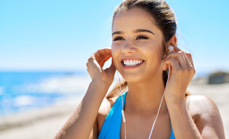 Earphones, fitness and happy woman by beach for running with music, podcast or radio online. Sport, tech and female athlete streaming workout playlist for cardio exercise for marathon training by seaの写真素材