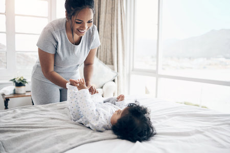 Mother, playful and dressing baby in home, love and parent tasks or responsibility for clean child. Mama, daughter and bonding with infant in bedroom, changing toddler and support kid with hygieneの写真素材