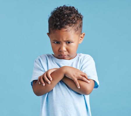 Child, portrait and sad with arms crossed in studio for tantrum, unhappy and moody for attention. Person, boy kid and angry face for drama, grumpy or disappointed on blue background with mockup spaceの写真素材