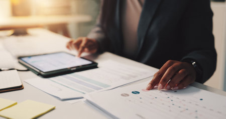 Person hands, tablet and documents in office for business, financial planning and data analysis at night. Woman, tech or paper with graphs for growth projection, company development or audit deadlineの写真素材