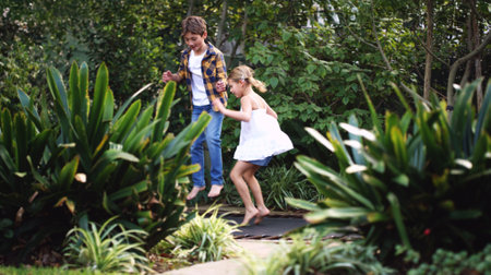 Trampoline, garden and kids with jump, energy and playground fun outdoor of home. Summer, fun and joy of siblings together with bounce, nature and holiday with youth and plants in backyard gameの写真素材