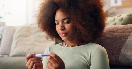 Pregnancy test, result and waiting with woman on in living room of home for detection or screening. Fertility, ivf and ovulation with pregnant person on floor in apartment for maternal anticipationの写真素材