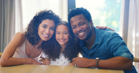 Interracial parents, girl and portrait in home with hug, smile and care with diversity or happy family. Father, mother and daughter with embrace, connection and love in living room for bondingの写真素材
