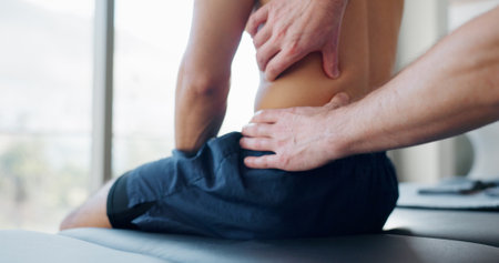 Hands, back pain and injury for massage with physiotherapy at clinic with recovery, process and relief for legs. Person, patient and help for ache, spine and rehabilitation for wellness at hospitalの写真素材