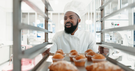 Muffin, bakery and cooking with black man in kitchen for coffee shop, food industry and breakfast. Shelf, chef and nutritionist with baker and dessert in restaurant for baking, cafe and orderの写真素材