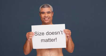 Portrait, smile and man with poster for body positivity in studio, acceptance or topless with space. Face, confident or mature person with sign for pride, size or self love message on dark backgroundの写真素材