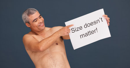 Smile, man and poster for body positivity in studio, acceptance or topless. Pointing, confident or mature person with sign for pride, natural size or self love message for advocacy on dark backgroundの写真素材