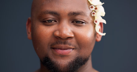 Portrait, skincare and black man in studio with flowers, confidence and natural self care in lgbt aesthetic. Nature, floral and male person with gay pride, creative dermatology and grey backgroundの写真素材