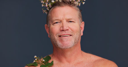 Beauty, flower crown and portrait of mature man in studio on dark background for natural skincare. Cosmetics, dermatology and smile with gay or queer person in floral wreath for antiaging wellnessの写真素材