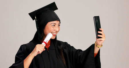 Woman, university graduation and happy with selfie and scroll for memories, profile picture and social media. Asian person, studio background and smile for certificate with celebration of achievementの写真素材