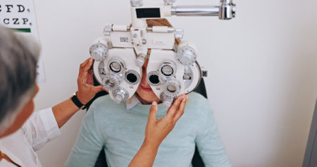 Doctor, optometry and woman on phoropter for vision, consultation and hands in clinic for health exam. Ophthalmologist, test and patient on machine for eye care, wellness and eyesight correctionの写真素材