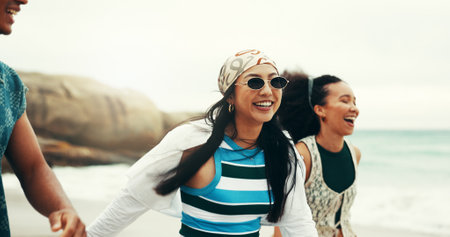 Excited, friends and walking on beach outdoor for travel reunion, summer vacation and laugh of funny joke. Smile, people and sunglasses for holiday journey, social gathering and weekend trip at oceanの写真素材