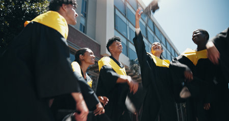 Celebration, graduation and throwing with group of friends outdoor on university campus together. College, smile and success with happy graduate or student people cheering for milestone goalsの写真素材