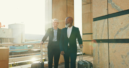 Team, business people and travel with luggage in city for journey, international trip or flight at airport. Suitcase, walking and mature professionals at building, hotel or talking outdoor on commuteの写真素材
