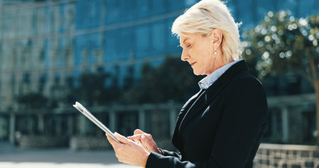Tablet, networking and mature businesswoman in city for email, connectivity or communication. Digital technology, research and female executive CEO with online contact for corporate deal in town.の写真素材