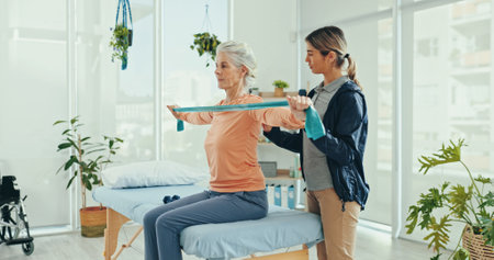Senior woman, physiotherapist and resistance band for stretching, recovery or support at hospital. Doctor, exercise and elderly patient with progress, guide and rehabilitation for injury at clinicの写真素材