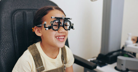Trial frame, smile or girl in eye test at optometry clinic for eyewear, retina health or sight wellness. Vision exam, excited or happy child in assessment for optical lenses, frames or spectaclesの写真素材
