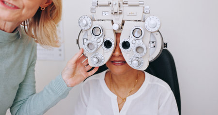 Doctor, optometry and woman on phoropter for eye care, consultation and hands in clinic for health exam. Ophthalmologist, test and patient on machine for vision check, wellness or eyesight correctionの写真素材