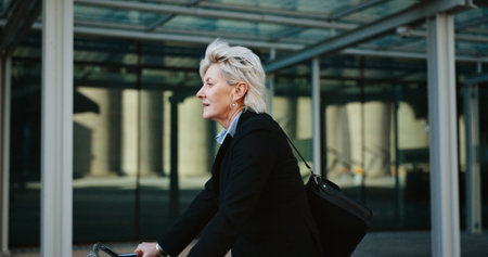 Bicycle, outdoor and mature businesswoman in city with travel, journey or trip to office building. Commuting, cycle and professional female executive with eco friendly transport to work in urban townの写真素材