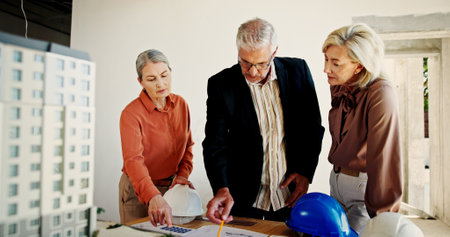 Mature architect, team and discussion with blueprint for construction project or remodeling. Group, engineer and document for building design, floor plan and people at meeting for development at siteの写真素材