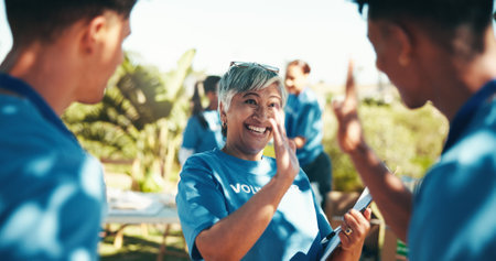 High five, volunteers and happy for charity, group and success of fundraiser, smile and mature woman. Outdoor, celebration and coordinator with good news for people, community service and nonprofitの写真素材