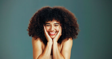 Portrait, beauty and excited woman with afro hair care, studio and treatment for wellness and health. Face, growth and happy model with smile, volume and natural texture on green background in Brazilの写真素材