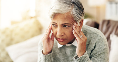 Stress, thinking and anxiety with old woman on sofa for mental health, depression and psychology. Reflection, frustrated and fear mindset with senior person at home for trauma, memory and doubtの写真素材