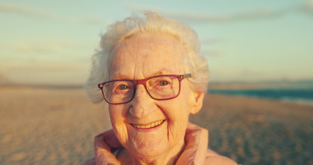 Portrait, elderly woman and smile by beach for retirement or holiday with health, outdoor and relax. Senior, female person and happiness as confident for vacation, wellness and adventure as pensionerの写真素材