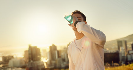 Man, sports drink and sunset with exercise, training and city for fitness or cardio workout. Athlete, person and electrolyte hydration on mountain for wellness, health and summer marathon performanceの写真素材