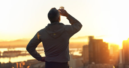 Man, drink and fitness with sunset of city for hydration, break or natural sustainability. Back, male person or active runner with mineral liquid or bevereage for thirst, rest or health and wellnessの写真素材