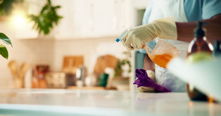 Person, hands or spray in home for cleaning, housekeeping or bacteria prevention. Cleaner, cloth or detergent bottle at kitchen counter for surface protection, service or disinfectant for hospitalityの写真素材