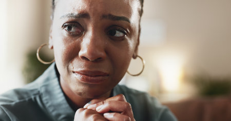 Crying, sad face and black woman with depression, thinking and psychological trauma in home living room. Tears, unhappy and African person with anxiety for crisis, mental health challenge and stressの写真素材